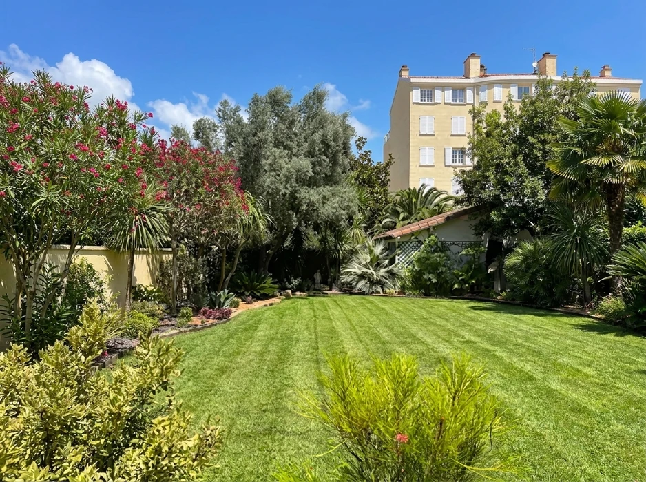 Jardin méditerranéen soigné avec pelouse rayée fraîchement tondue, bordures plantées d'oléandres en fleurs roses, palmiers, agaves et oliviers argentés
