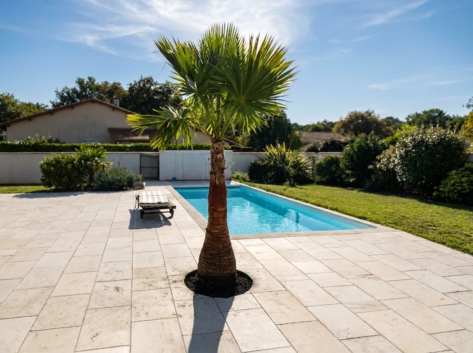 Terrasse en travertin beige entourant une piscine rectangulaire aux eaux turquoise, avec un transat en bois