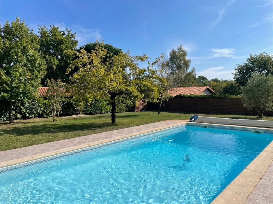 Piscine rectangulaire extérieure aux eaux turquoise, entourée d'un dallage en pierre beige