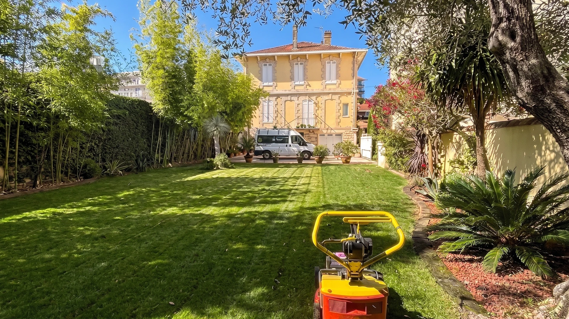 Jardin paysager luxuriant avec piscine couverte d'un volet roulant immergé, entourée d'une terrasse en bois composite avec transats blancs
