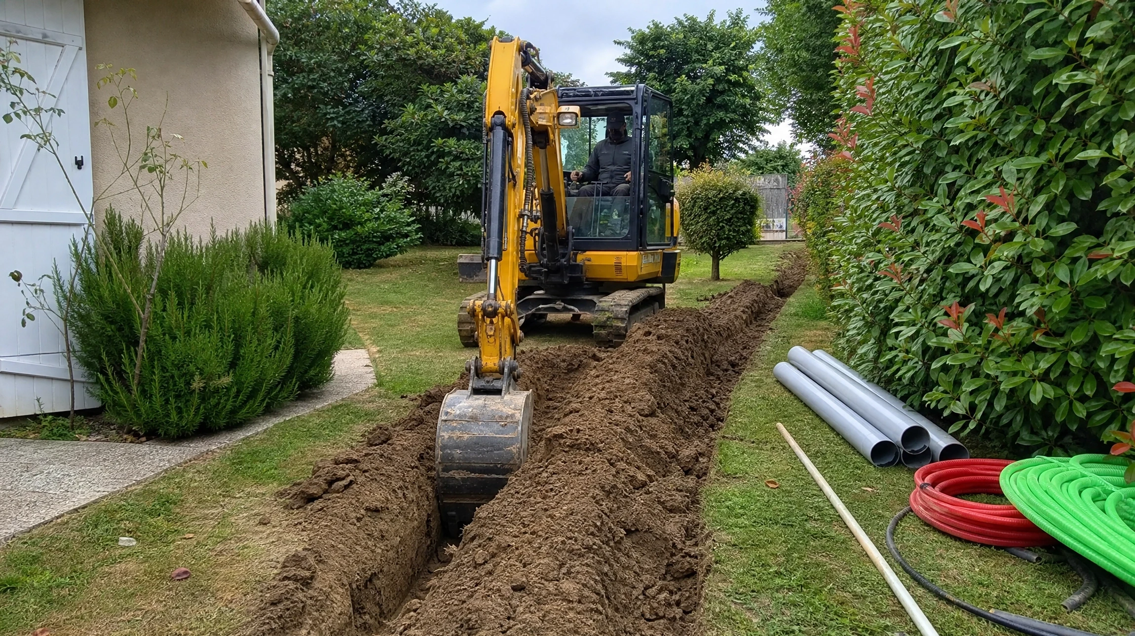 Chantier de terrassement résidentiel avec mini-pelle jaune en action dans jardin privé